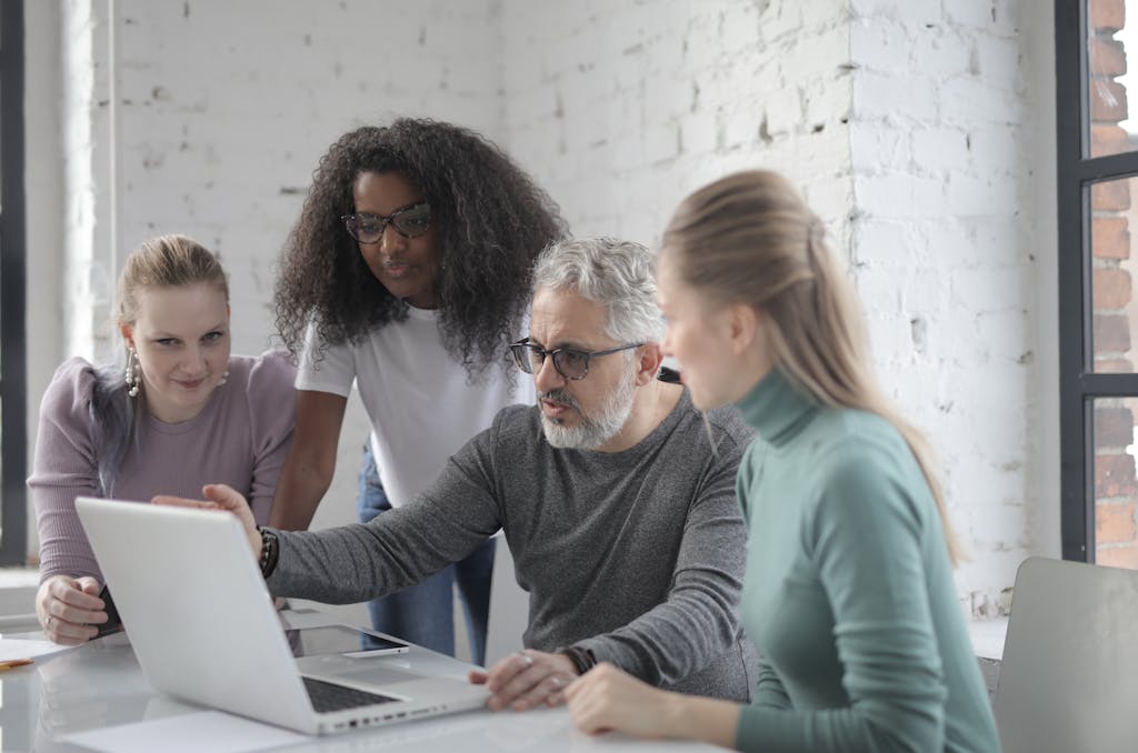 Focused bearded man sitting at table and working with laptop while discussing business project with colleagues and explaining details of ideas