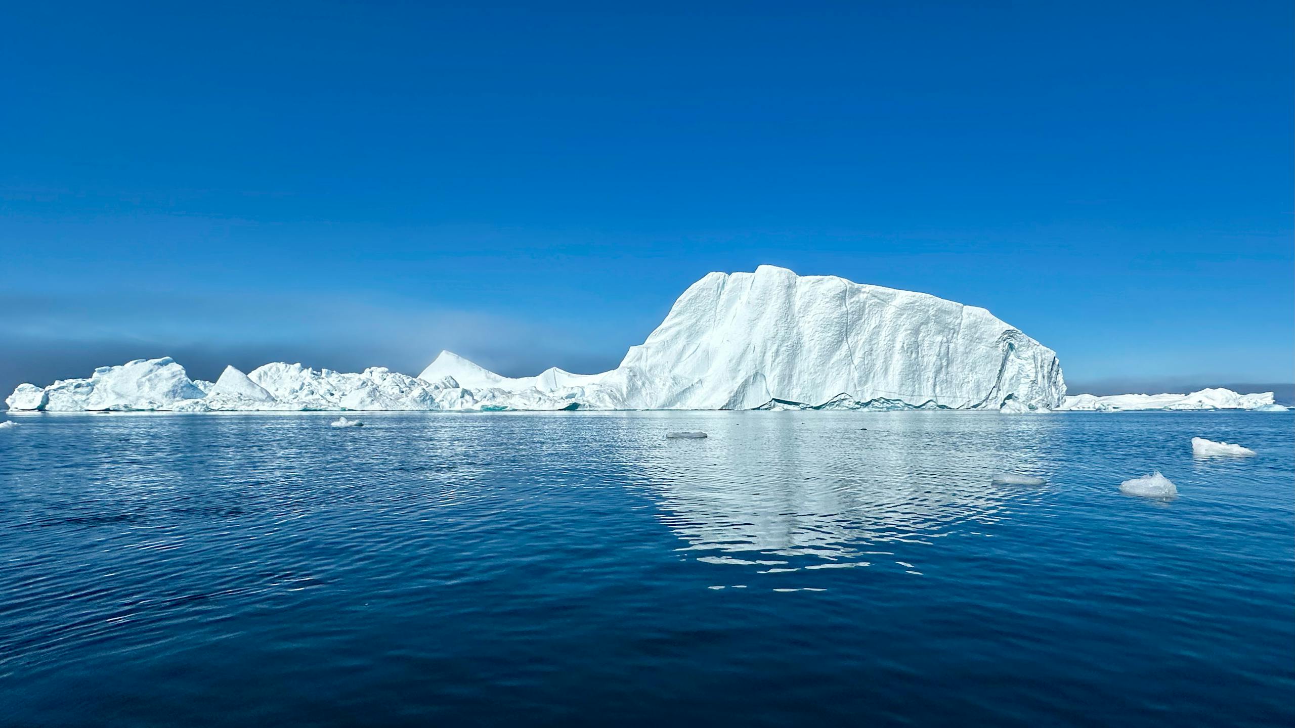 Beautiful iceberg reflecting in the calm waters of Greenland under a clear blue sky.